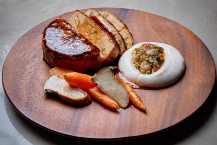 Wooden board plating of food featuring meat, vegetables and dip.