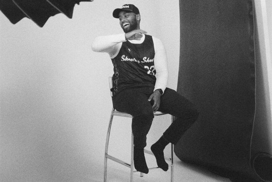 Photojournalism image of a man seated on a stool in a photographer's studio, laughing.