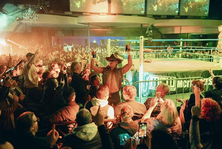 A large crowd watching a wrestling match with once man standing in front of the crowd with his hands up. 