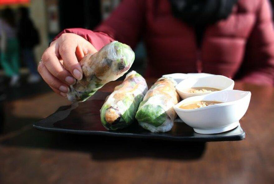 A hand picking up a rice paper roll from a plate.