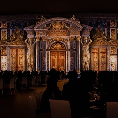 A darkened dining space with illuminations on the walls resembling Versailles at Château Merveilles.