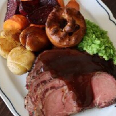 A white oval plate with roast beef, veggies, Yorkshire pudding and gravy.