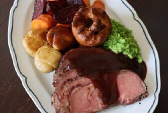 A white oval plate with roast beef, veggies, Yorkshire pudding and gravy.