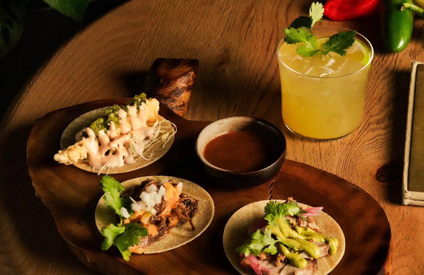 A spread of three tacos, a dipping sauce and margarita.