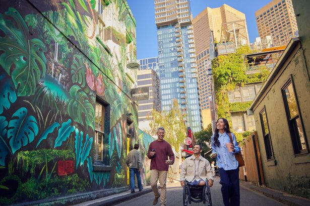 Four people in a laneway with a large wall mural of a jungle.