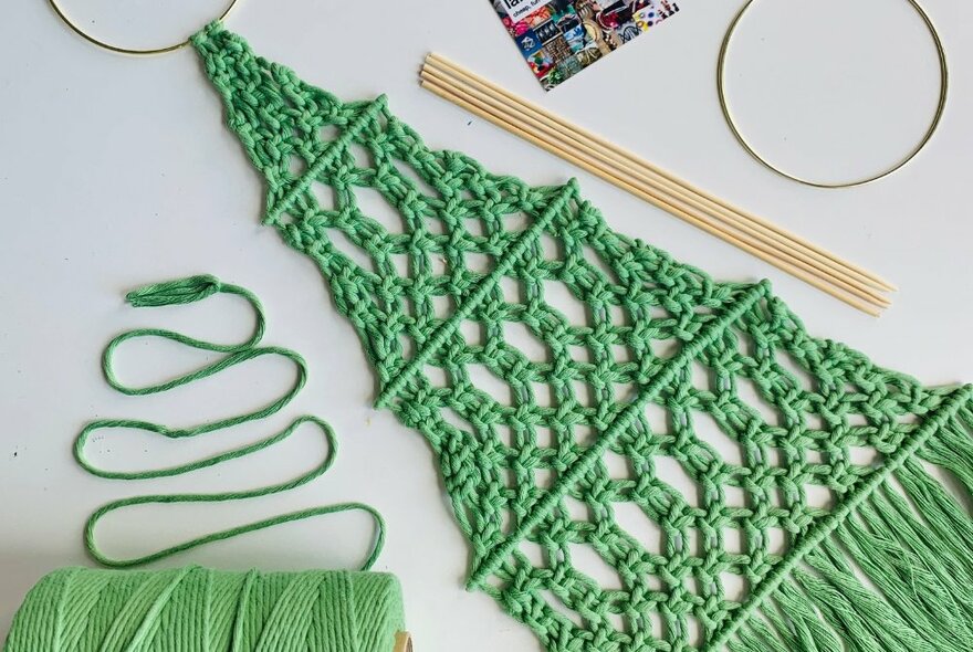 Looking down at a table at a cone of green yarn, a green macrame flat Christmas tree, some simple tools.