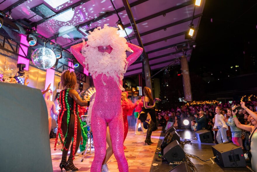 The main stage at Fed Square at night, filled with performers in colourful costumes, performing in front of an audience.
