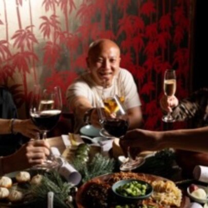 People celebrating and seated around a table of food and wine in a restaurant.