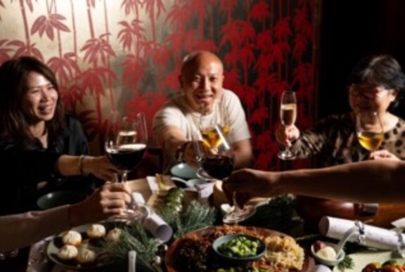 People celebrating and seated around a table of food and wine in a restaurant.