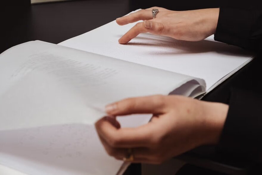 Hands holding a book open, one handing tracing words on a page.