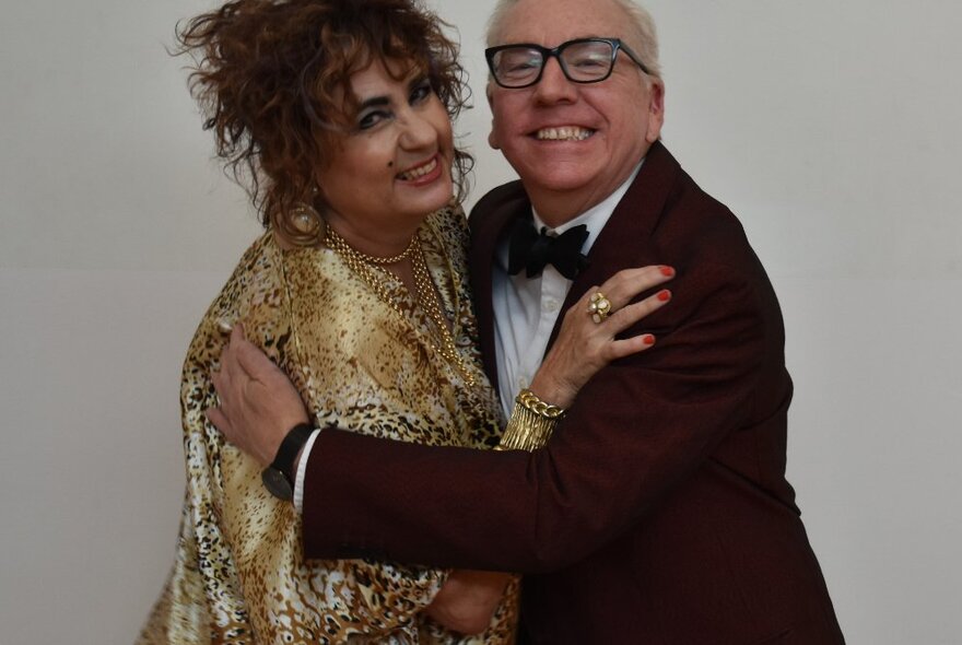 Middle-aged actor and actress arm in arm wearing evening dress, man in tuxedo, woman wearing a gold gown.