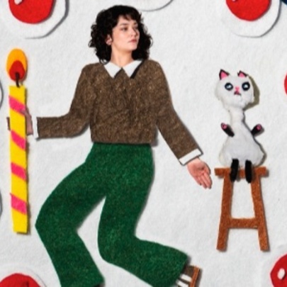 Felt cut-out themed picture of a woman on a pizza with cut-out tomatoes and a cat on a stool.