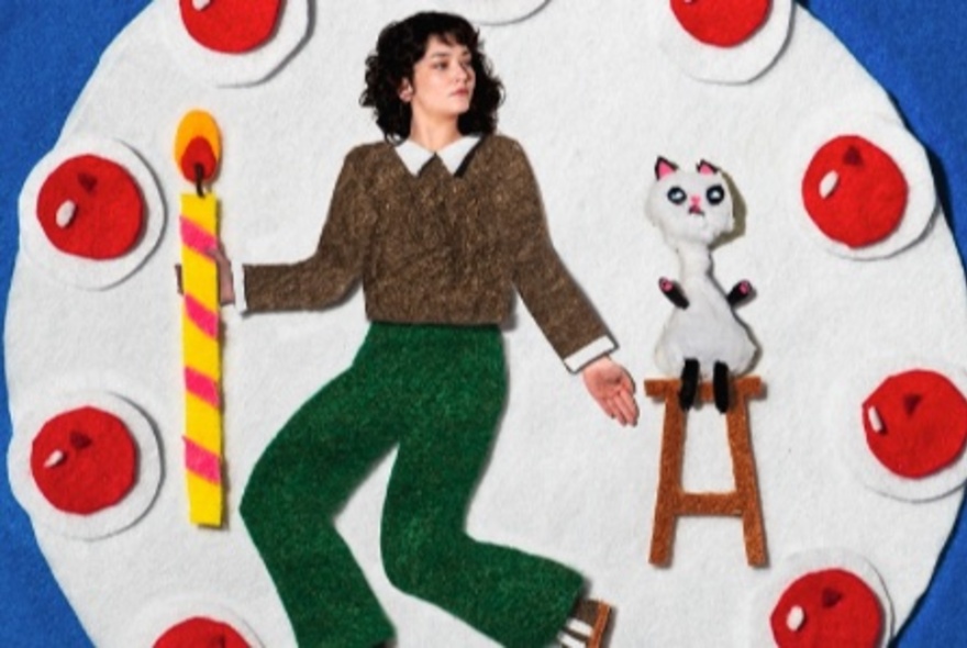 Felt cut-out themed picture of a woman on a pizza with cut-out tomatoes and a cat on a stool.