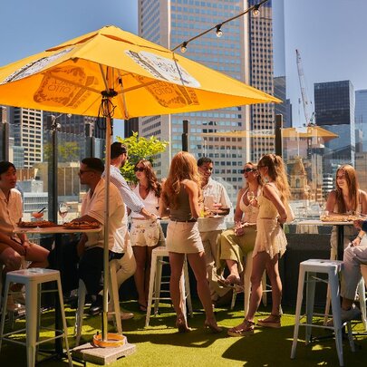 Young people enjoying the sunshine at a rooftop bar in Melbourne, the city skyline in the background.