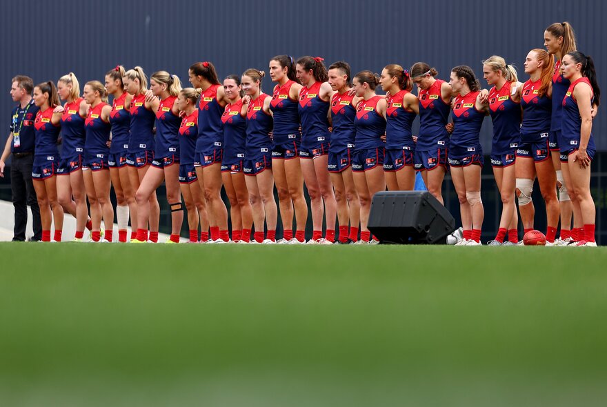 Melbourne AFLW team standing in a row on the ground at the start of a match.