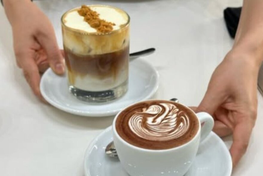 Hands holding two coffee drinks.