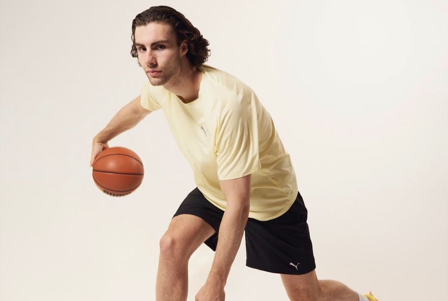 A basketballer in a yellow t-shirt and black shorts bouncing a basketball with his right hand.