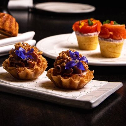 Delicate savoury pastries, topped with edible flowers, arranged in pairs on white plates.