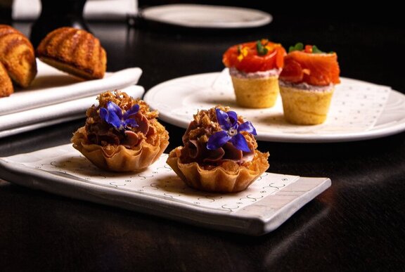Delicate savoury pastries, topped with edible flowers, arranged in pairs on white plates.