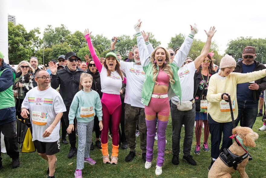 Group of people on a fundraising walk or run, raising their arms and smiling in an outdoor setting.