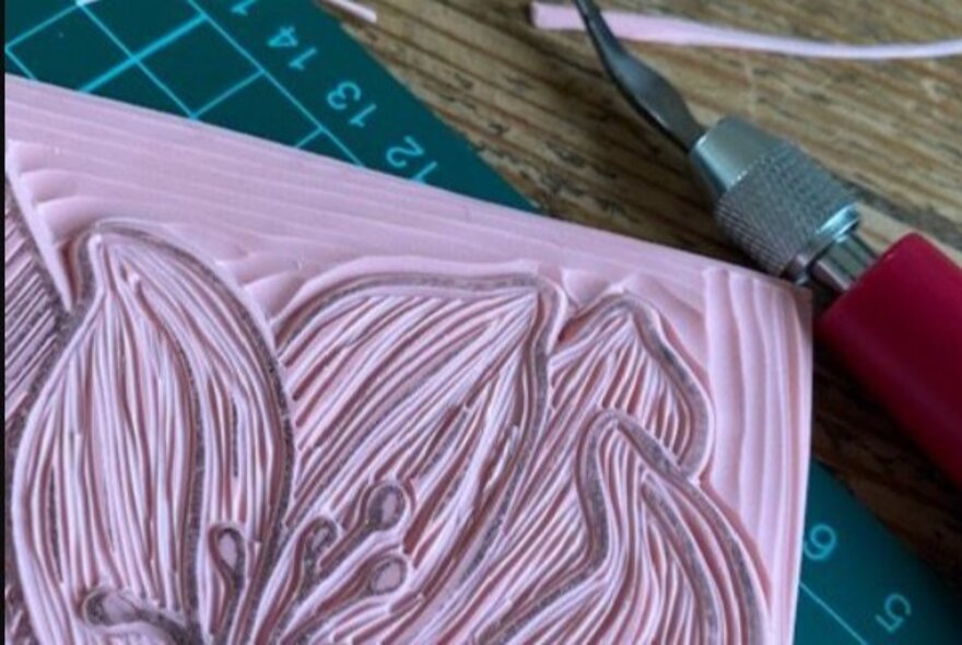 A linocut being created in purple with a tool and a cutting board.