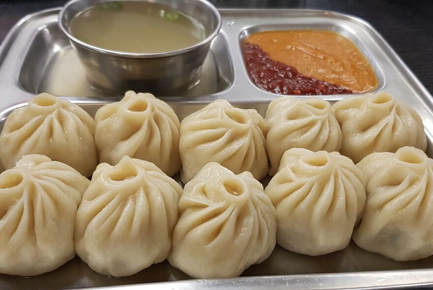 A tray with ten dumplings and dipping sauces. 