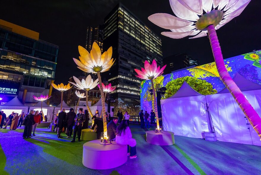 A festival in the city at night with giant colourful lotus flower sculptures.