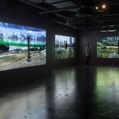Inside a large, darkened gallery space with projected artwork on the walls and a single person viewing.