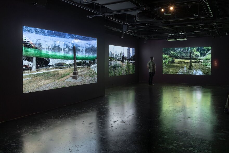 Inside a large, darkened gallery space with projected artwork on the walls and a single person viewing.