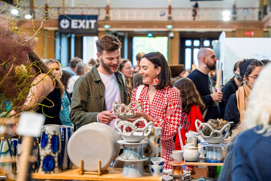 People browsing a designer craft stall and talking to the stallholder at the Big Design Market inside the Royal Exhibition Building.