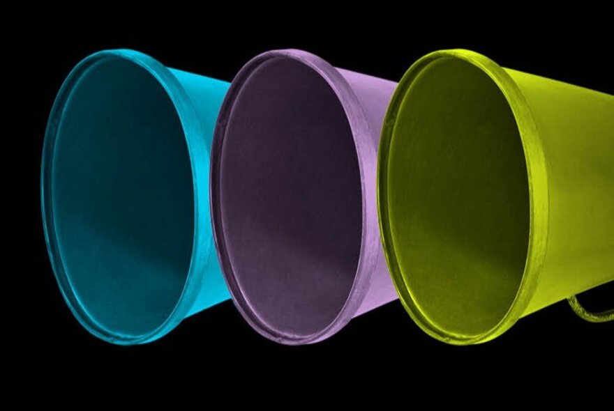 Three megaphones in a row, saturated in the colours of blue, purple and green, against a black background.