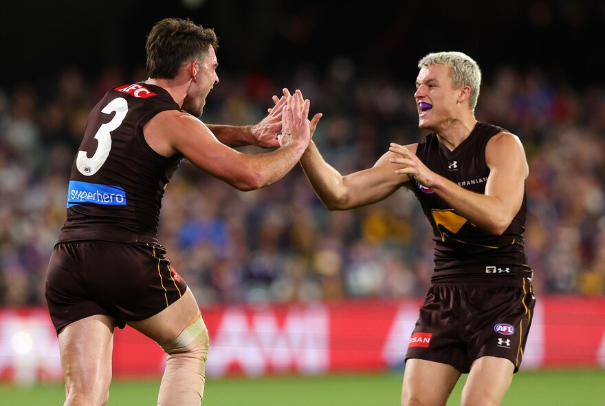 Two AFL football players cheering and giving each other high fives on the field during a match.