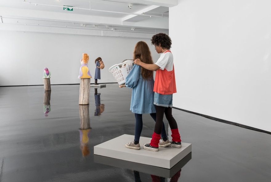 Installation view of Patricia Piccinini's exhibition of free standing sculptures and figures inside Tolarno Gallery, on a highly polished black concrete floor, set against white walls.
