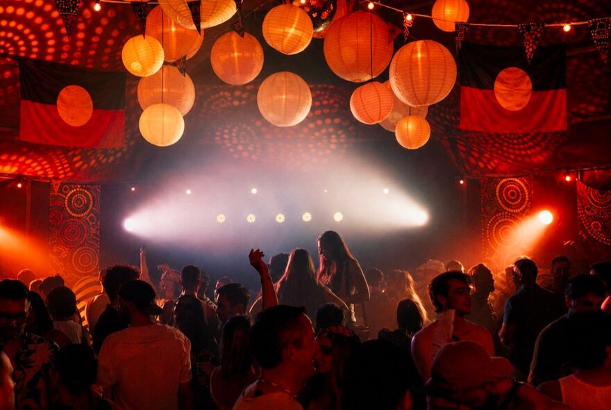 A darkened nightclub space with chinese lanterns and aboriginal artwork patterns on the wall and Aboriginal flags hanging from the ceiling.