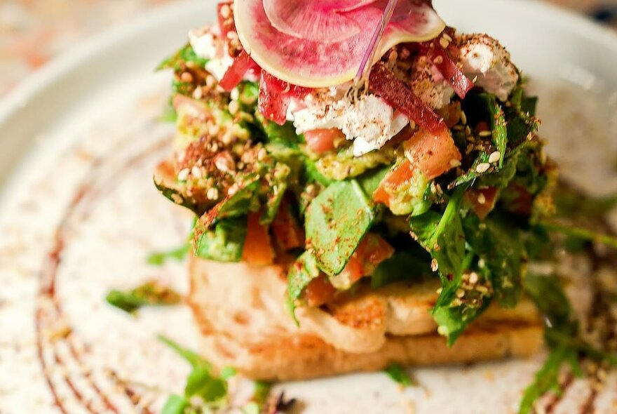 A toast stack with a mix of cooked and fresh ingredients on a round plate.