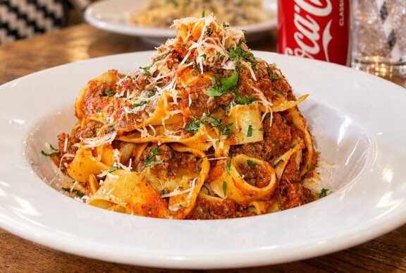 A bowl of pasta with a Bolognese sauce, garnished with grated parmesan cheese.