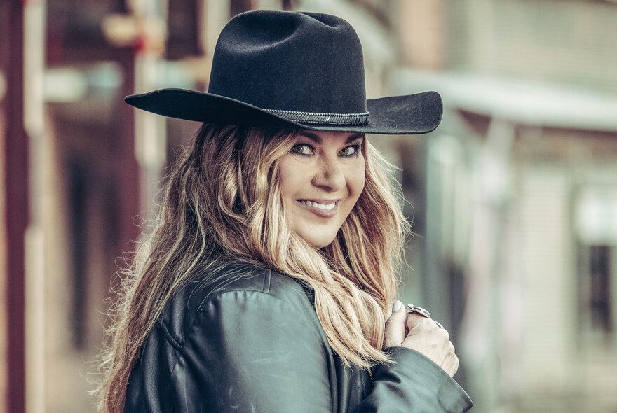 Portrait of singer/songwriter, Sandy Facee, wearing a leather jacket and black cowboy hat, her long hair draped over her shoulder.