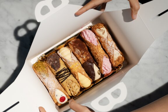 A person opening a tasting box with six different cannoli inside.