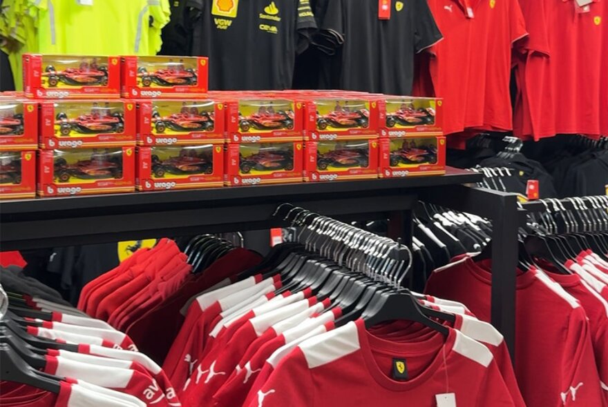 Racks of red F1 Ferrari branded shirts and model cars on display in a shop.