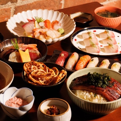 Array of Japanese food in different sized ceramic bowls and plates, on a small wooden dining table.