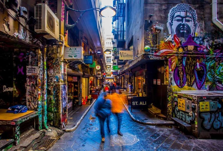 Blurred people walking through a heavily graffitied laneway. 