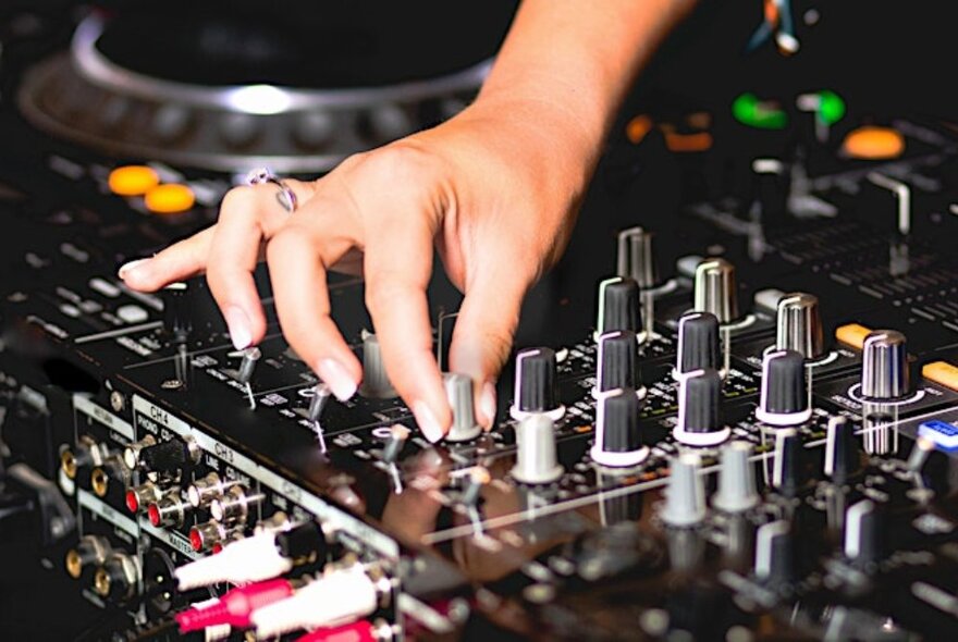 A hand twirling a control dial on a DJ mixing console.