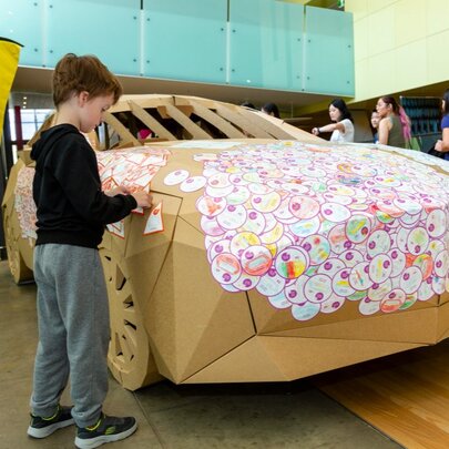 A child putting stickers on The Big (Safe) Cardboard Car, a life-size educational car installation at the Melbourne Museum.