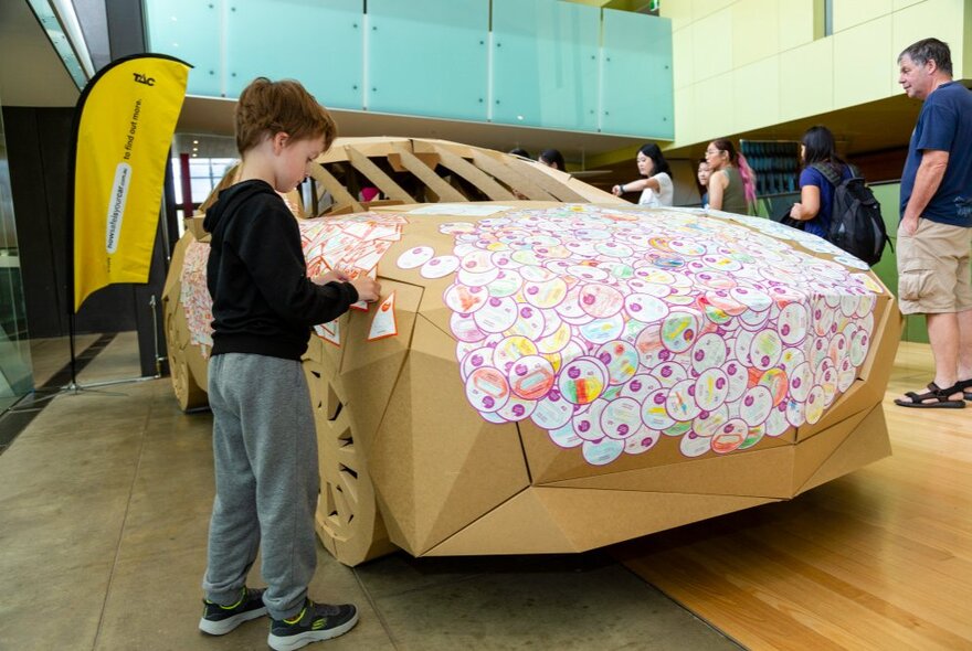 A child putting stickers on The Big (Safe) Cardboard Car, a life-size educational car installation at the Melbourne Museum.