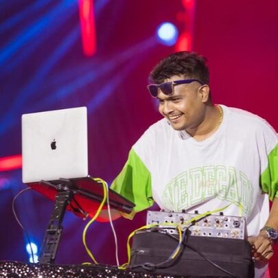 A smiling DJ performing in front of a MacBook with sunglasses on his forehead.
