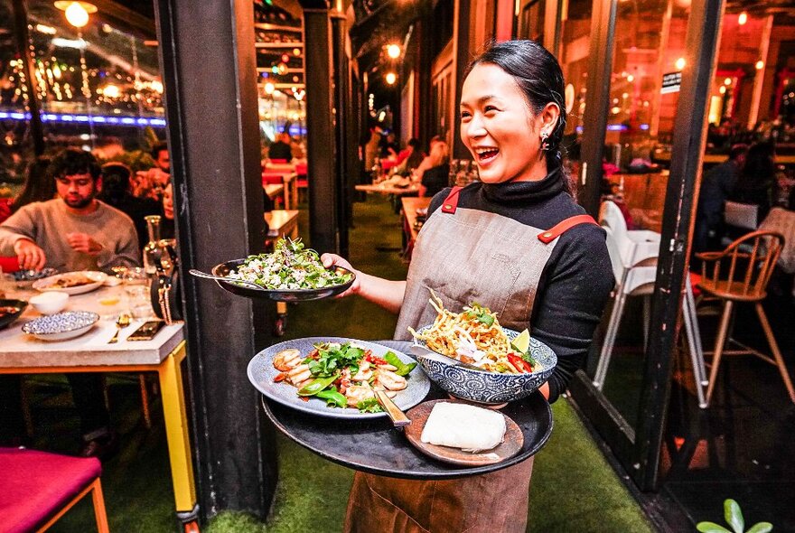 A smiling waitress presents dishes on food on a tray. 