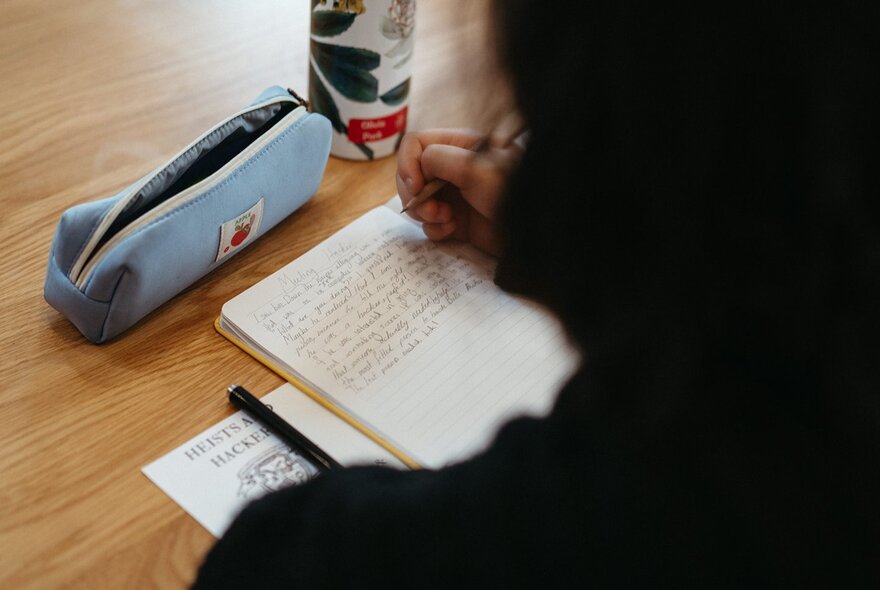 Child seated at a table writing in a notebook.