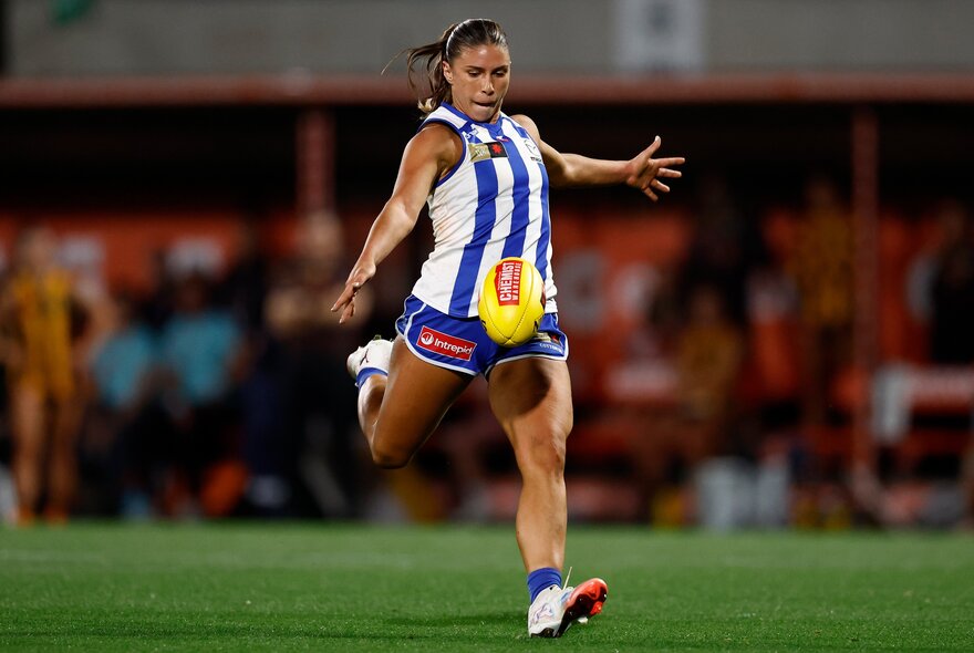 North Melbourne AFLW player kicking the ball during a match.