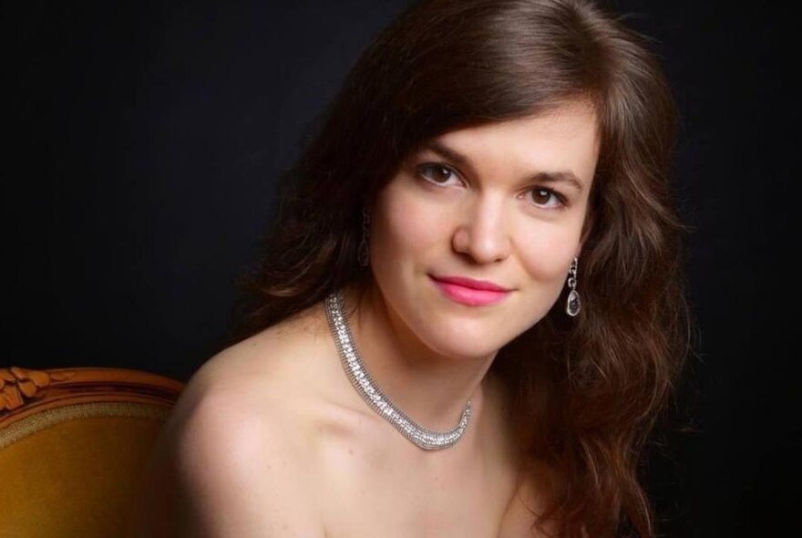Woman with long dark hair, parted on the side, wearing a strapless gown and glittering necklace.