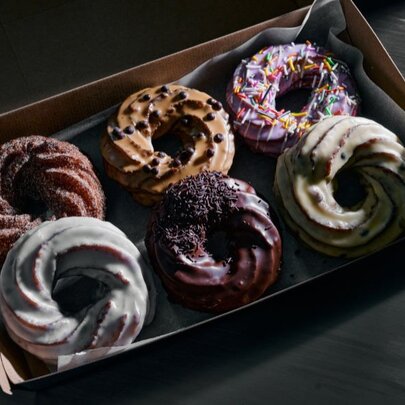 A take-away box of six crullers, all with different flavoured icing.
